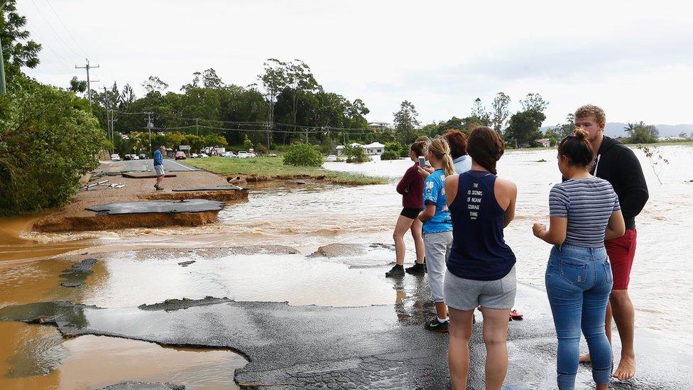 Residents stand next to a washed-away road.