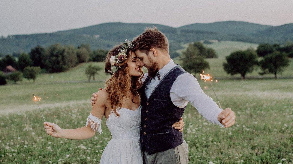 A man and a woman at their wedding holding sparklers in a field