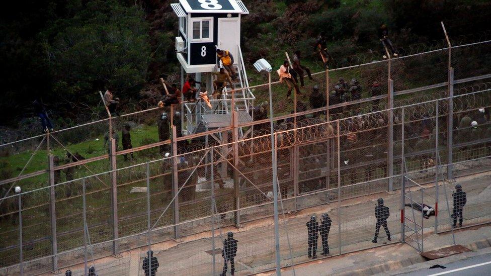 African migrants sit on top of a border fence during an attempt to cross into Spanish territories, between Morocco and Spain"s north African enclave of Ceuta, December 9, 2016