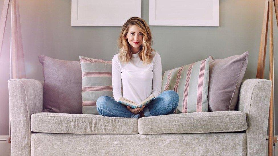 Zoella sitting on the sofa with a book