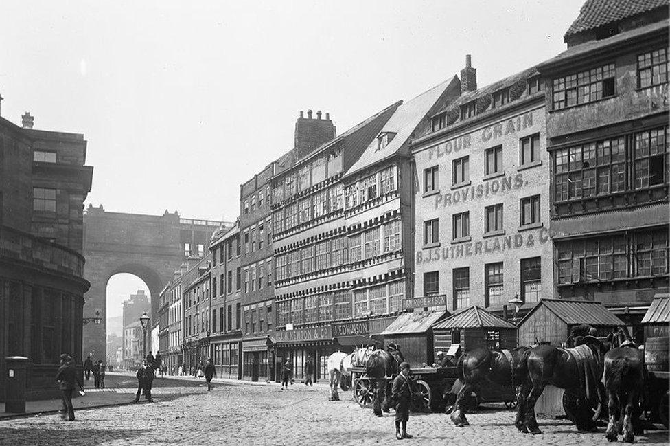 Black and white view of horses standing outside buildings