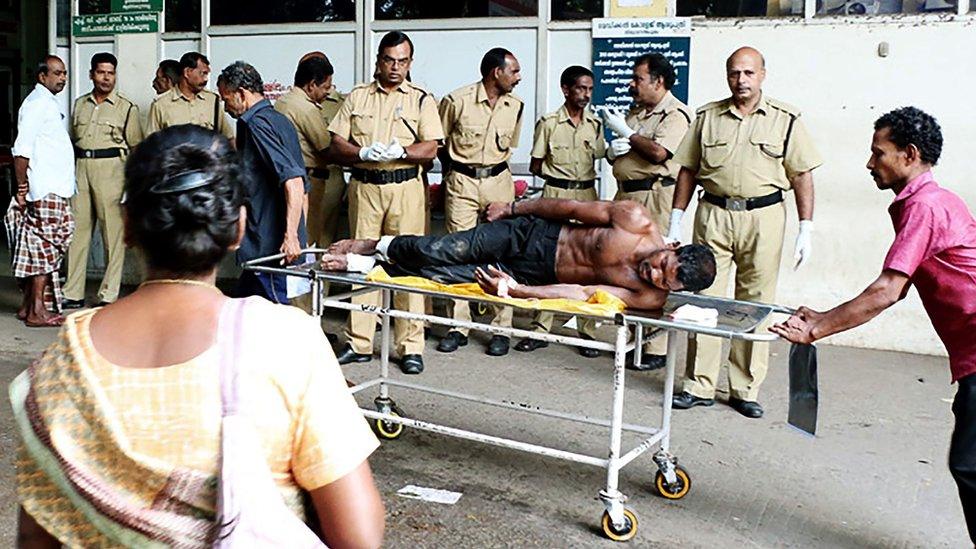 Indian medical officials use a trolley to transport an injured man from a vehicle into a hospital in Paravur