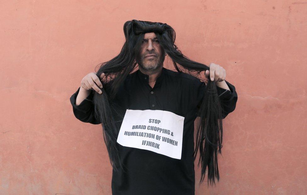 Ahsan Antoo wears a wig of long hair while holding a sign that says "stop braid chopping and humiliation of women" in Kashmir