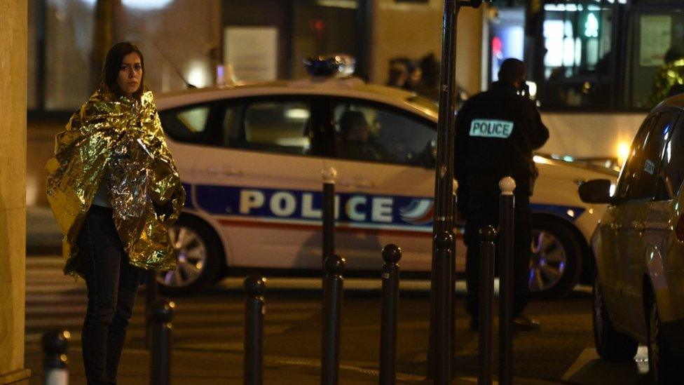 A woman wrapped in a life emergency blanket stands near the Bataclan concert hall in central Paris, on 14 November, 2015.