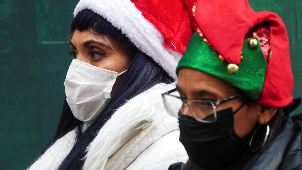 People wearing festive hats and masks walk through Times Square in New York City, on 15 December 2021