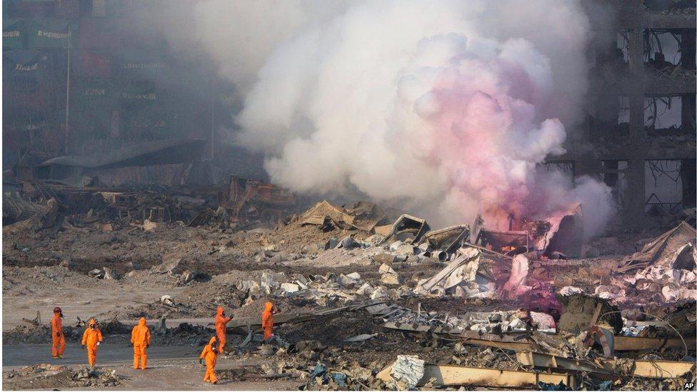 Firefighters in protective gear watch partially pink smoke continue to billow after an explosion at a warehouse in Tianjin (13 August 2015)