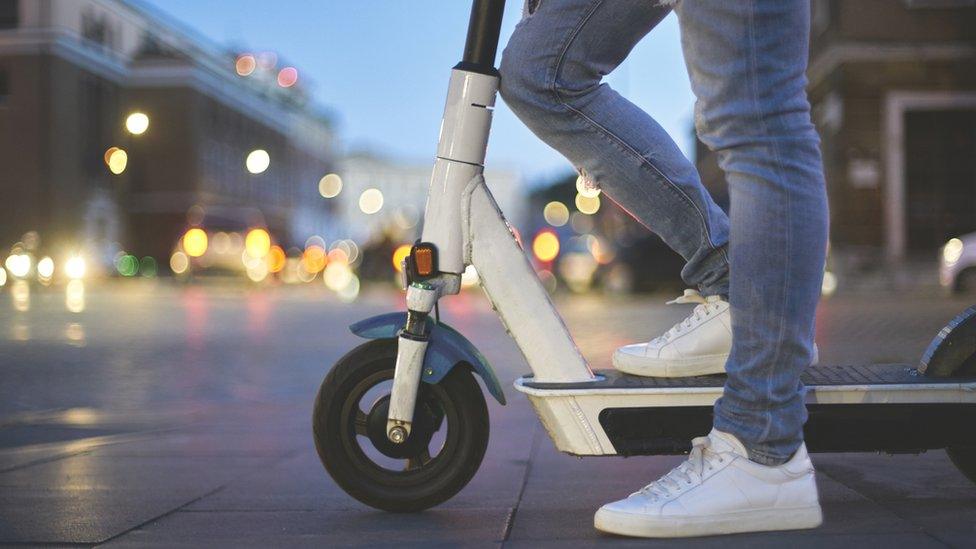 Low section of man riding electric push scooter. Traffic street lights on background.