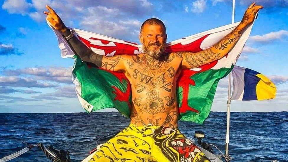 Matt Pritchard at sea holding a Welsh flag