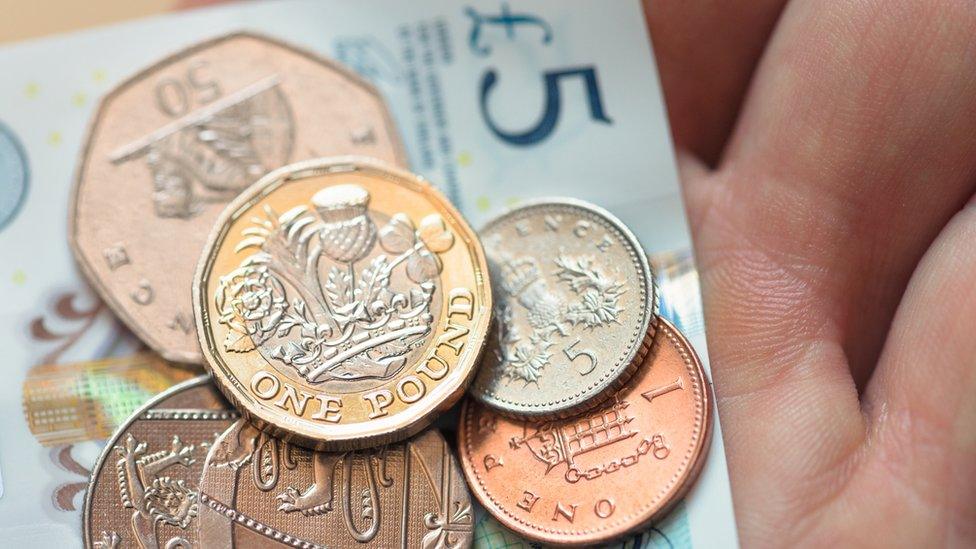 A selection of coins lie on top of a five pound note held in someone's hand