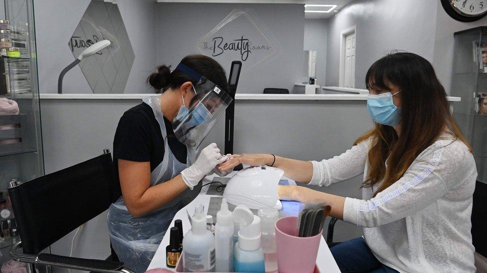 Nail technician Hannah Jones wears a PPE face shield and mask as she paints the nails of customer Lynsey Scott at The Beauty Rooms in Oxton, Birkenhead