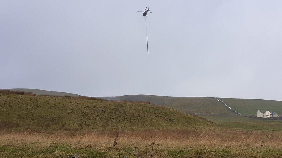 Helicopter carries new pole above countryside