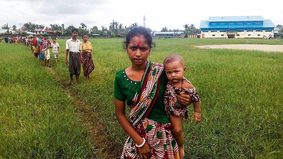 A woman holds a child in her arms as she arrives at the Yathae Taung township in Rakhine, Myanmar, after fleeing from violence in her village, 26 August