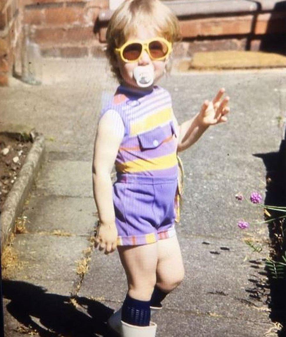 Nicola Williams aged three posing in shorts, sunglasses and wellington boots.