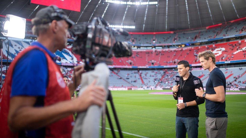 A cameraman films presenters on the side of Bayern Munich's pitch