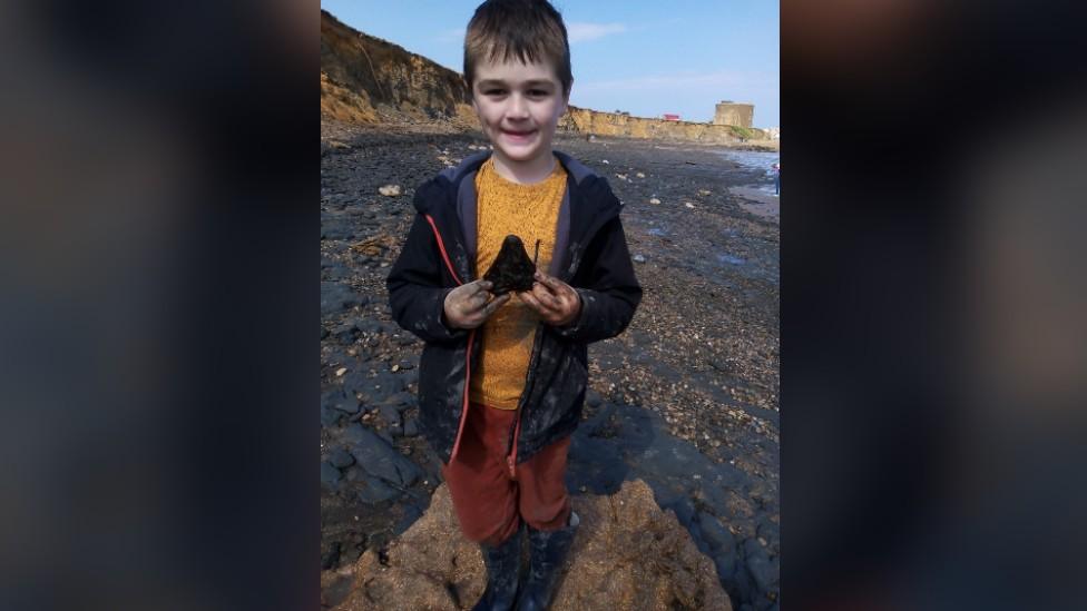 Sammy Shelton holding a shark's tooth on a beach