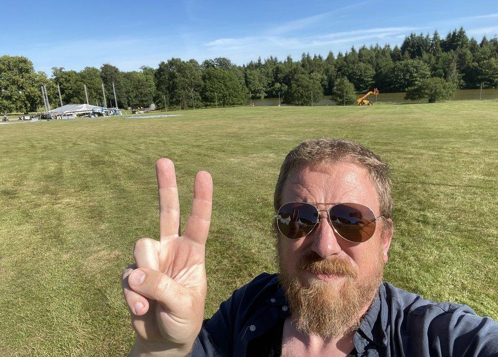 Greg Wells poses in front of the partially-built main stage at the Bigfoot festival in Warwickshire