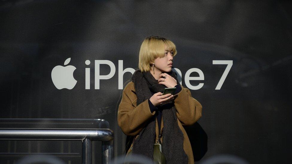 Chinese woman with phone in front of iPhone logo