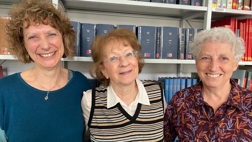 Three women stand with their arms around each other