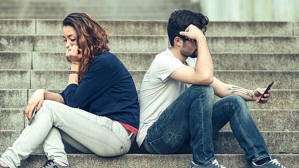 teenage couple sitting back to back on phones