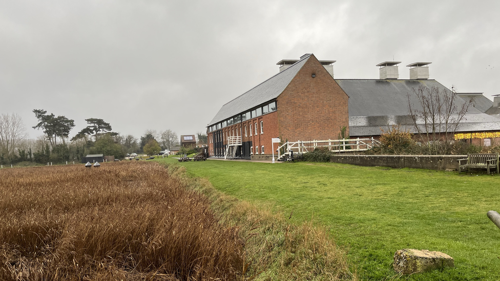 The banks of an estuary, with a two-storey maltings building to the right.