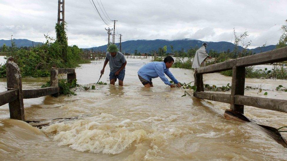 This picture from the Vietnam News Agency taken on 11 October 2017 shows men wading through a flooded area in the central province of Nghe An