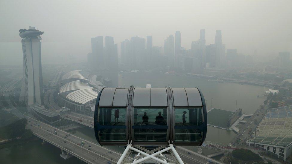 Tourists sit in a capsule on the Singapore flyer observatory wheel overlooking the skyline of the central business shrouded by haze in Singapore September 10, 2015