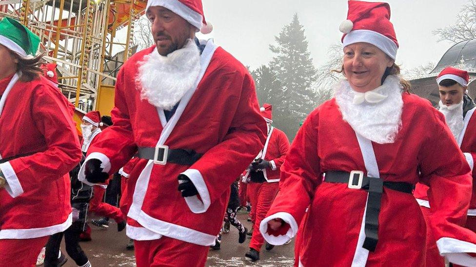 A man and a woman in Santa outfits running with the group