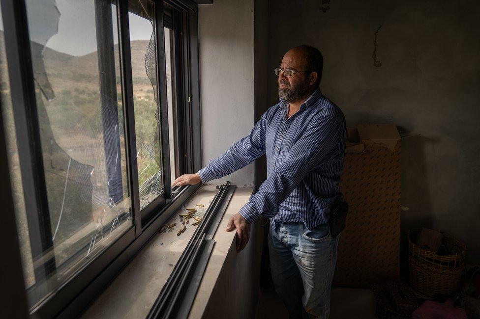 Abdellatif looks out from a broken window in his home. Bullet shells, collected from where the settlers fired on the house, sit in front of him.