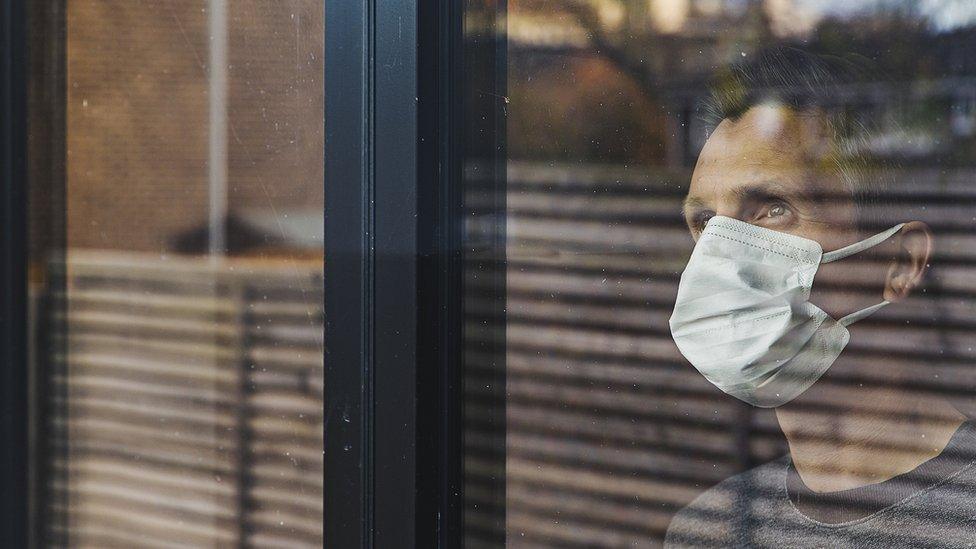 man looking through window wearing mask