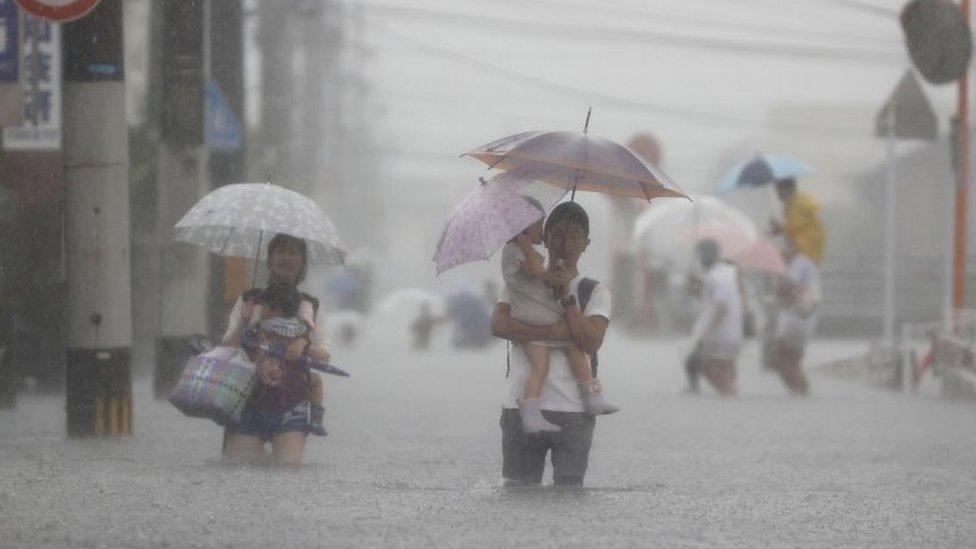 Local residents walk in a road flooded by heavy rain in Kurume, Fukuoka prefecture, western Japan