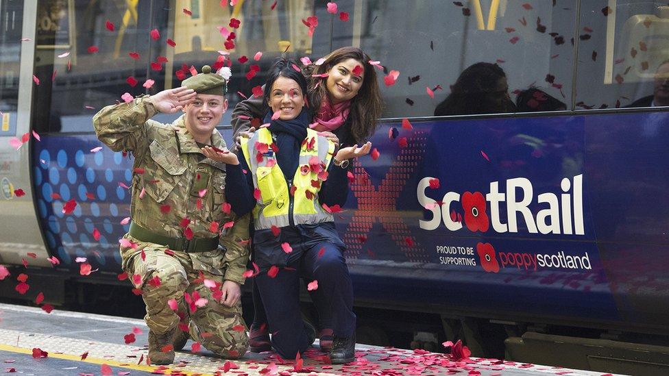 three people pose by a poppy logo on a train