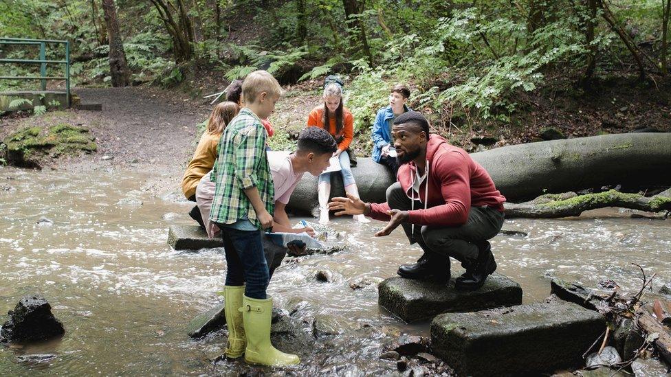 Group of young people by a river, being taught by an adult