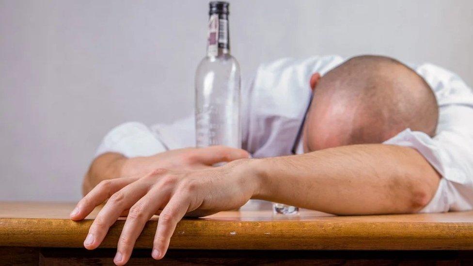 Man collapsed on a table holding an empty glass bottle