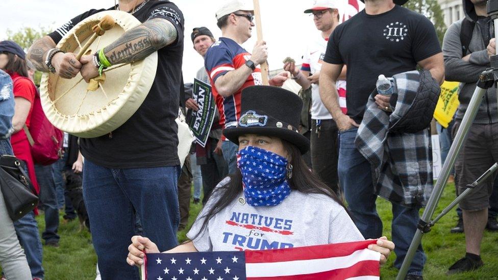 Covering her face with a red, white and blue scarf and holding a flag, Susan Keen (C) attends a "Hazardous Liberty! Defend the Constitution!" rally to protest the stay-at-home order, at the Capitol building on 19 April 2020 in Olympia, Washington