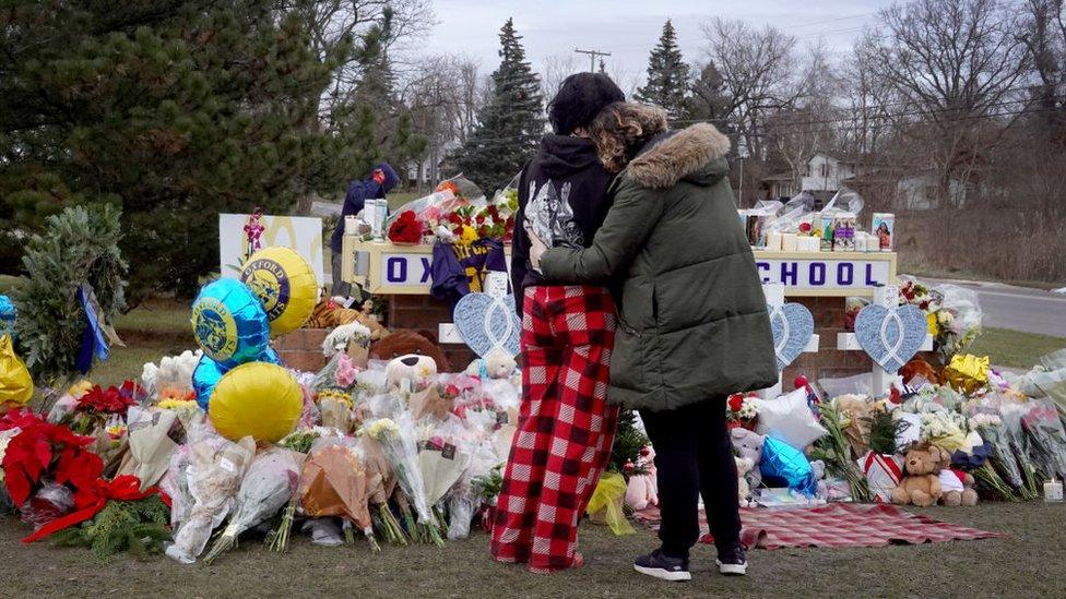 Memorial and flowers outside the school as two friends hug