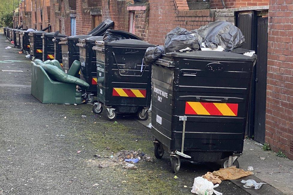 Old sofa and rubbish in backstreet next to communal bins