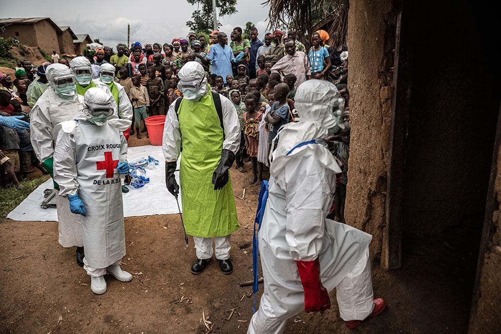 Neighbours and Red Cross burial workers in protective clothing gather outside a home