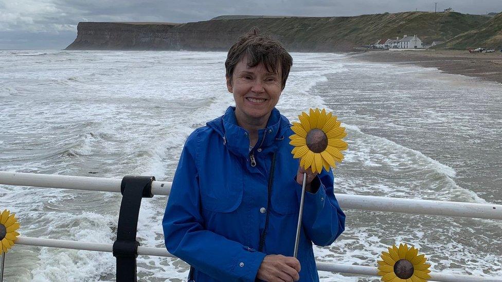 Karen Griffith standing on Saltburn Pier, holding the sunflower dedicated to her mum