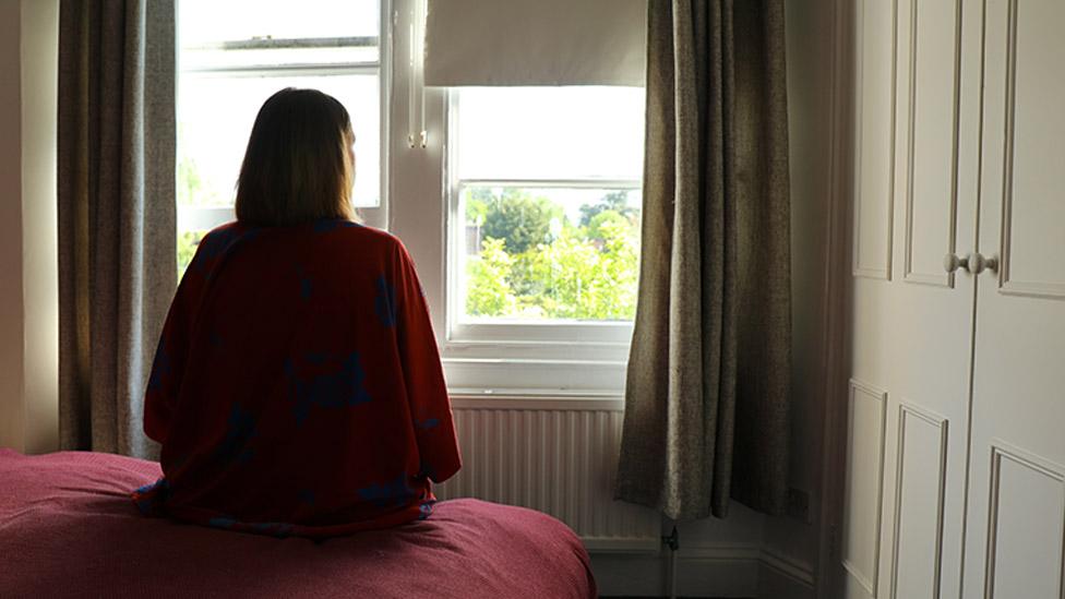 Lone woman sitting on the bed looking out of the window