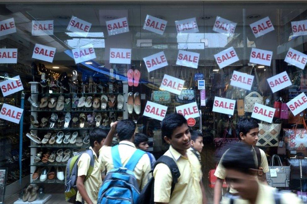 Indian schoolchildren stand in front of a store window offering discounts in Mumbai on August 3, 2016