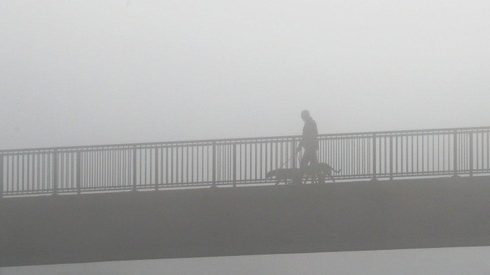 A man walking his dog in foggy conditions