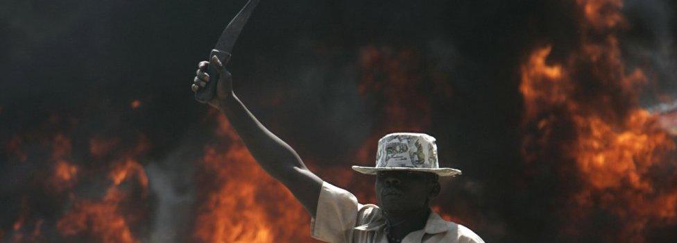 A supporter of the Orange Democratic Party holds up a machete in front of a burning barricade, Saturday, Dec. 29, 2007 during riots in the Kibera slum in Nairobi.