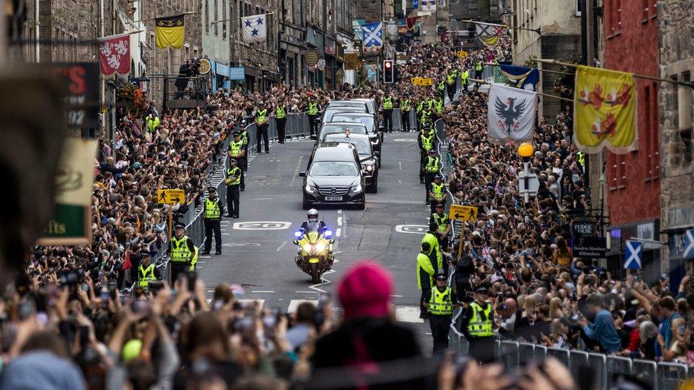 Members of the public gather on the Royal Mile in Edinburgh to watch the hearse carrying the coffin of Queen Elizabeth II passes by