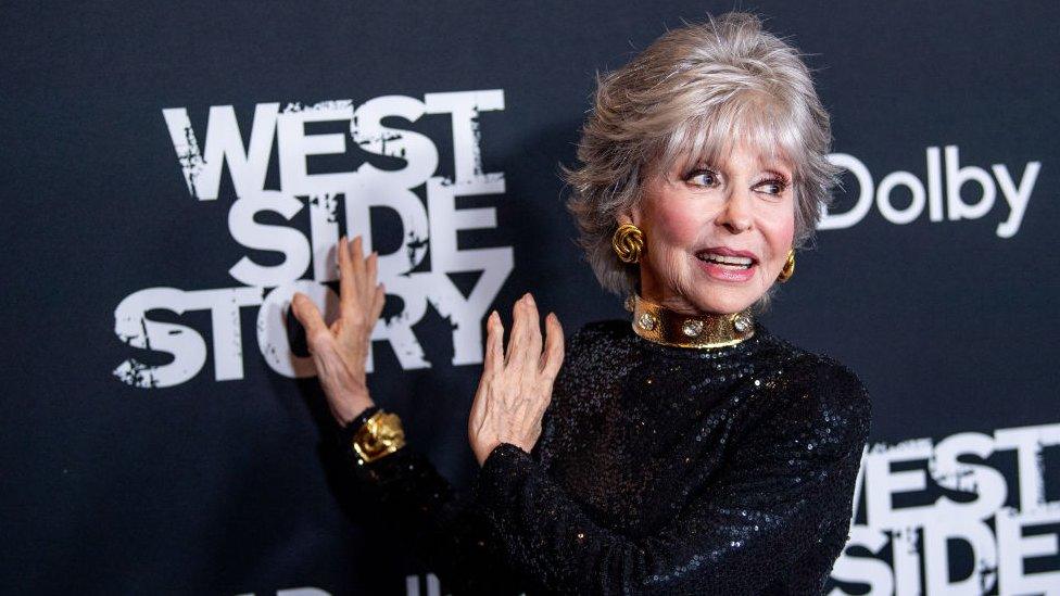 Rita Moreno standing in front of a sign reading, West Side Story