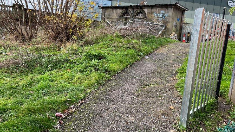 Part of shingle path alongside grass with open metal gate