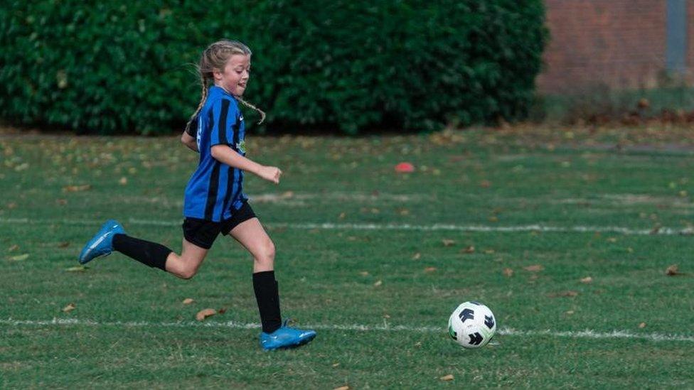 Lola, in a blue and black striped kit, playing football in Bedford