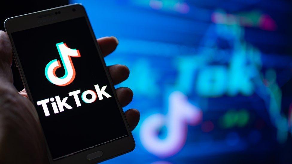 A person holding a phone displaying the TikTok logo