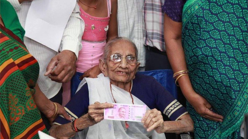 Indian Prime Minister, Narendra Modi"s mother Heera Ba Modi (C) holds up a 2,000 rupee note after exchanging money at a bank in Rysan village, near Gandhinagar, some 30 kms from Ahmedabad on November 15, 2016.