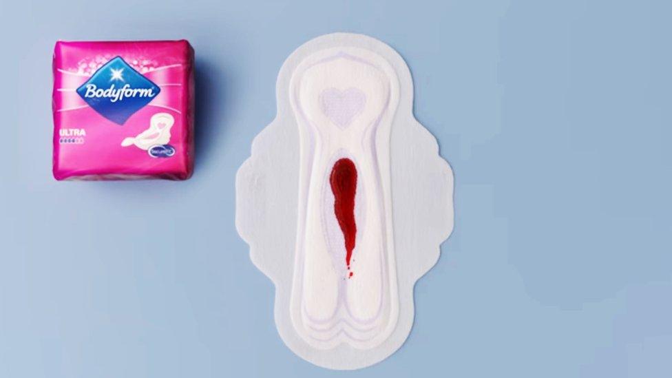 A packet of Bodyform sanitary towels places next to an open one with blood-like liquid on it