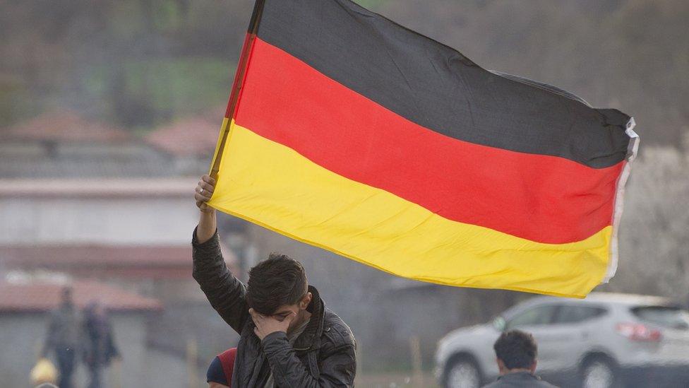 A migrant holds a German flag at the northern Greek border station of Idomeni (06 March 2016)